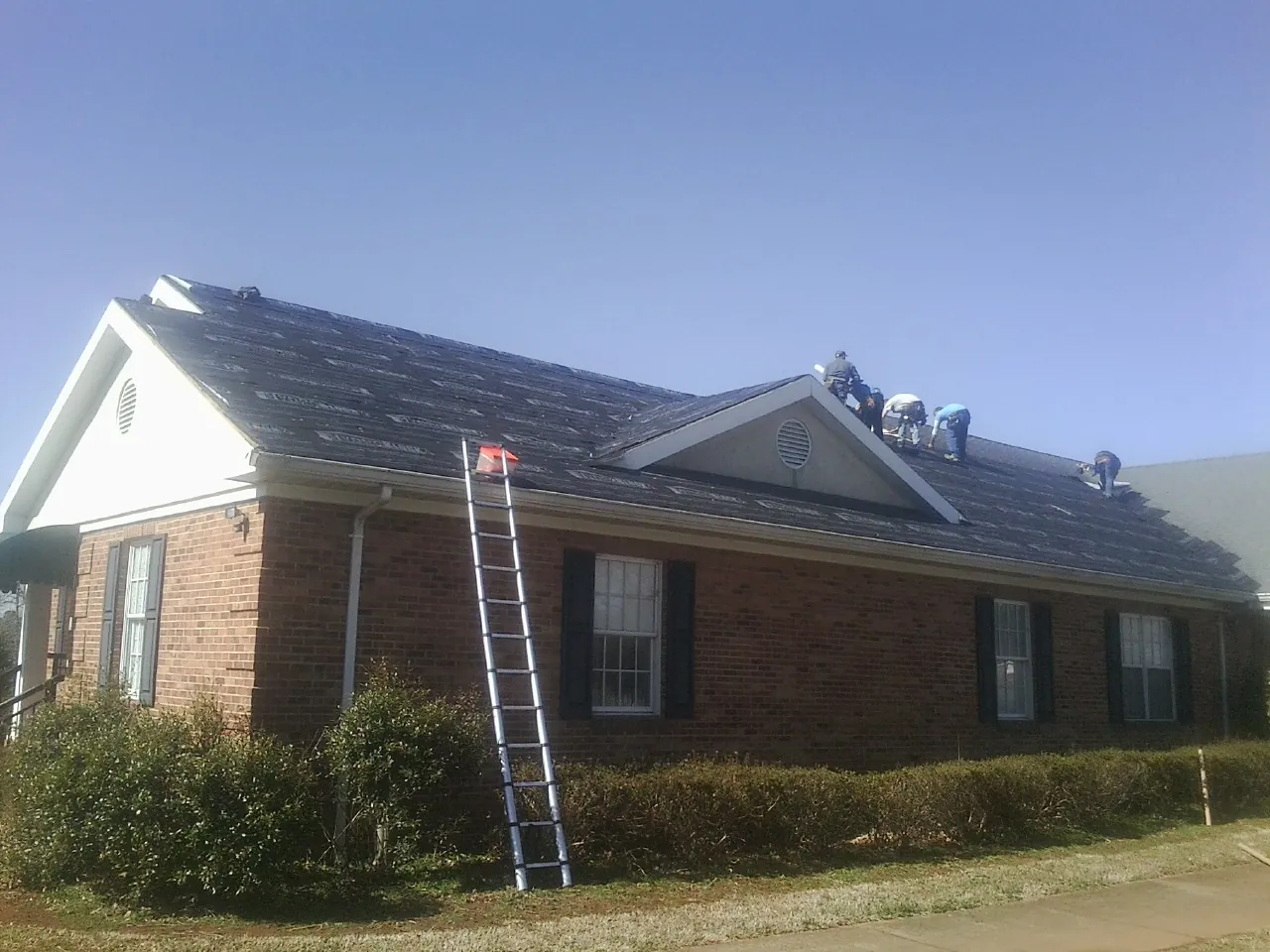 Crew tearing shingles off a brick ranch roof with a ladder set — Metal Roof Repair work by our crew in Keyport