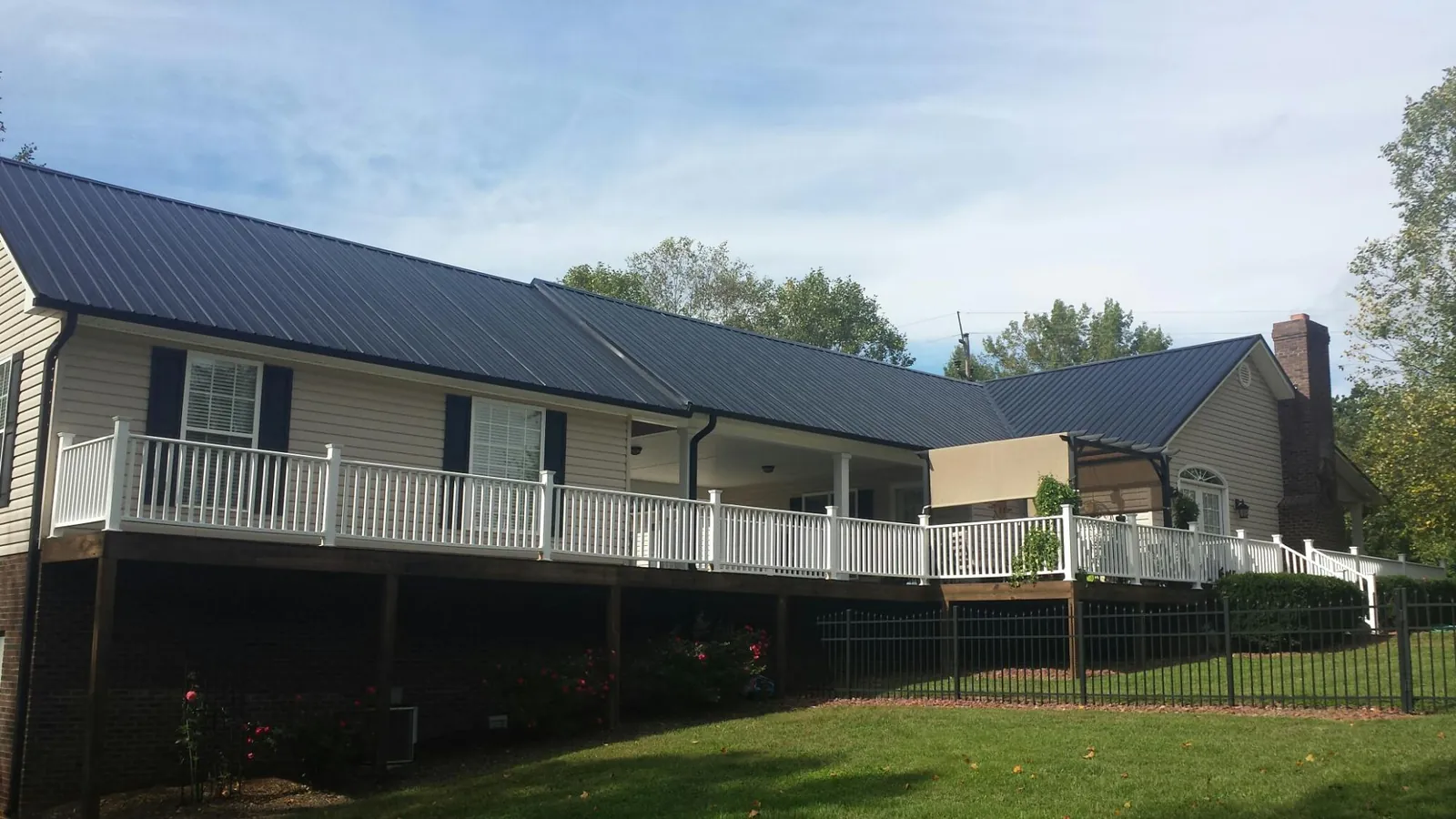 Black metal roof above a long white railed deck on a hillside home in Keyport